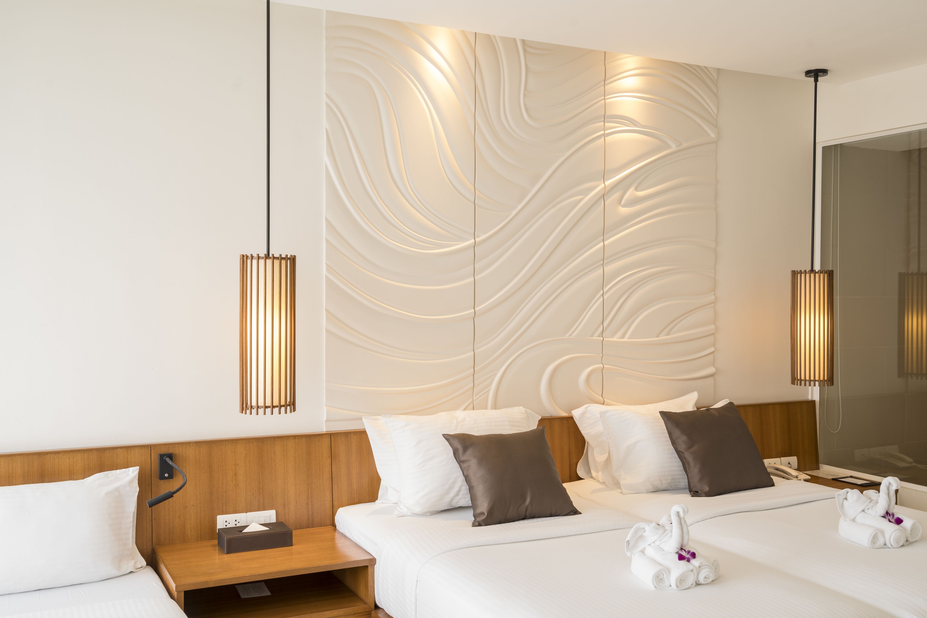 Una habitación de hotel moderna con una cama grande, un cabecero de madera, una mesita de noche con una lámpara y una pared con diseño texturizado.
