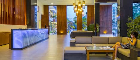 A modern lobby with a reception desk, seating area, and large windows.