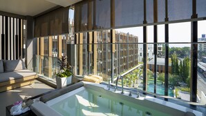 Een moderne hotelkamer met een groot raam, een balkon, een bank, een badkuip en uitzicht op de stad.