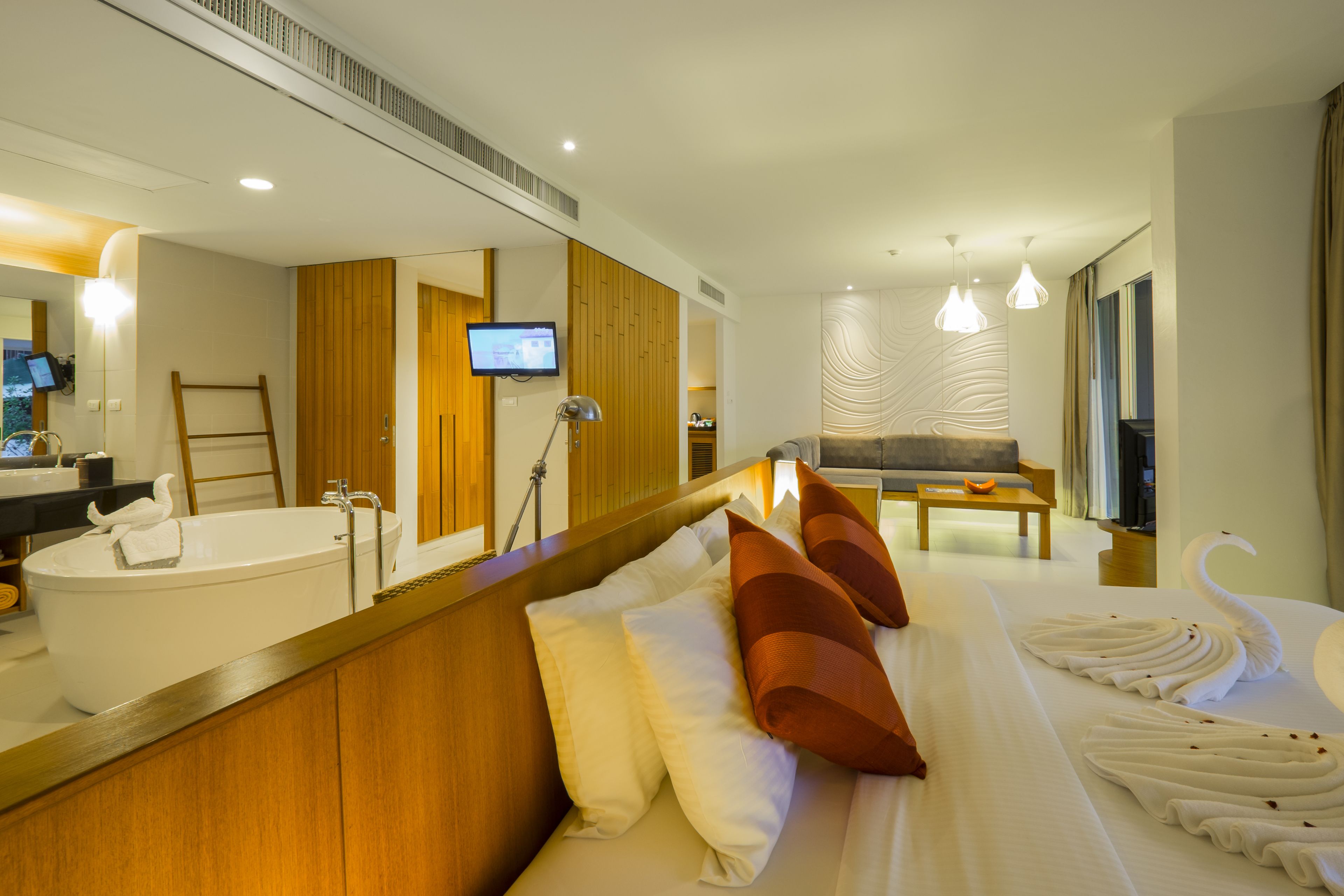 Ein modernes Hotelzimmer mit einem großen Bett, einem Badezimmer mit Badewanne, einem Fernseher und einer Wandpaneele aus Holz.