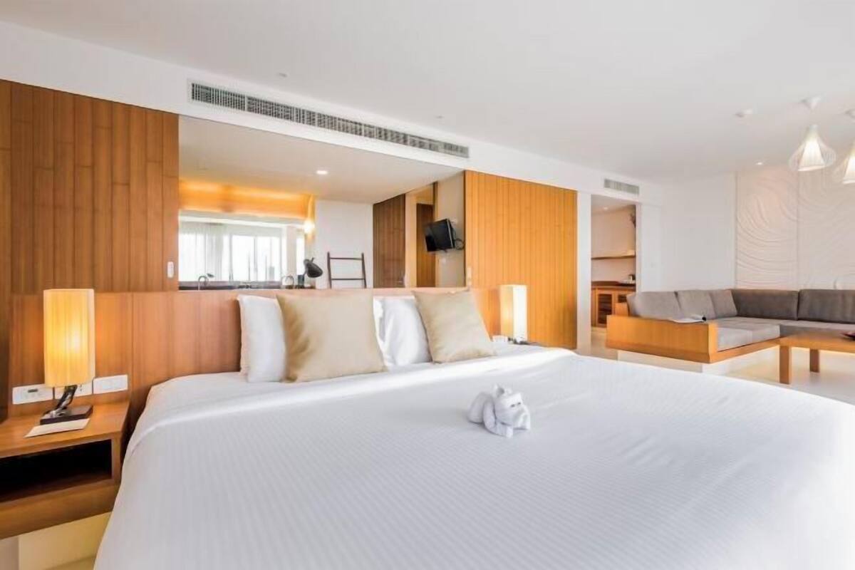 Une chambre d’hôtel moderne avec un grand lit, une tête de lit en bois, un canapé et une télévision.