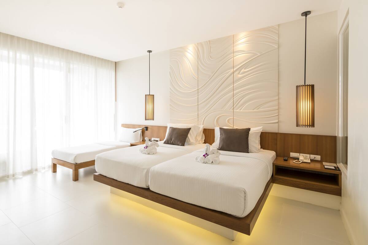 Une chambre d’hôtel moderne avec deux lits, une tête de lit en bois, une table de chevet avec une lampe et un mur au motif texturé.