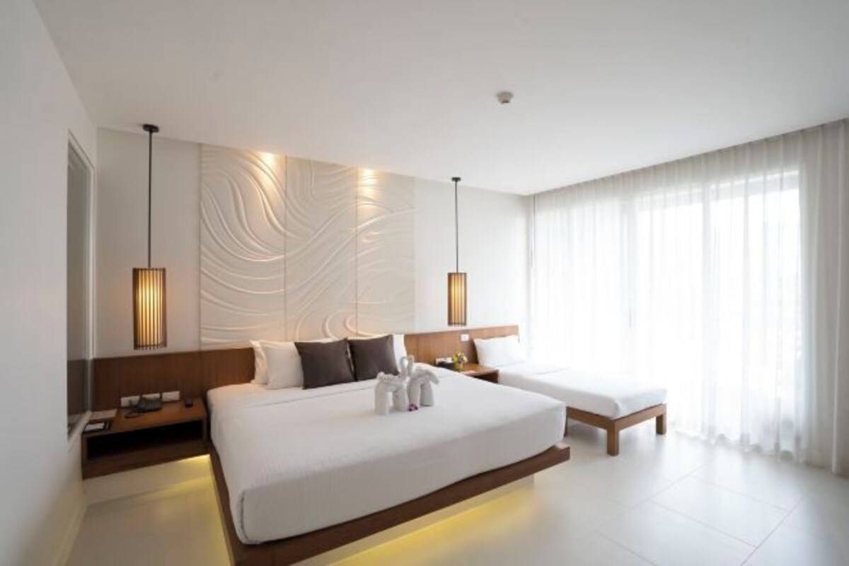 Una habitación de hotel moderna con una cama grande, mesitas de noche y vistas al exterior a través de cortinas translúcidas.