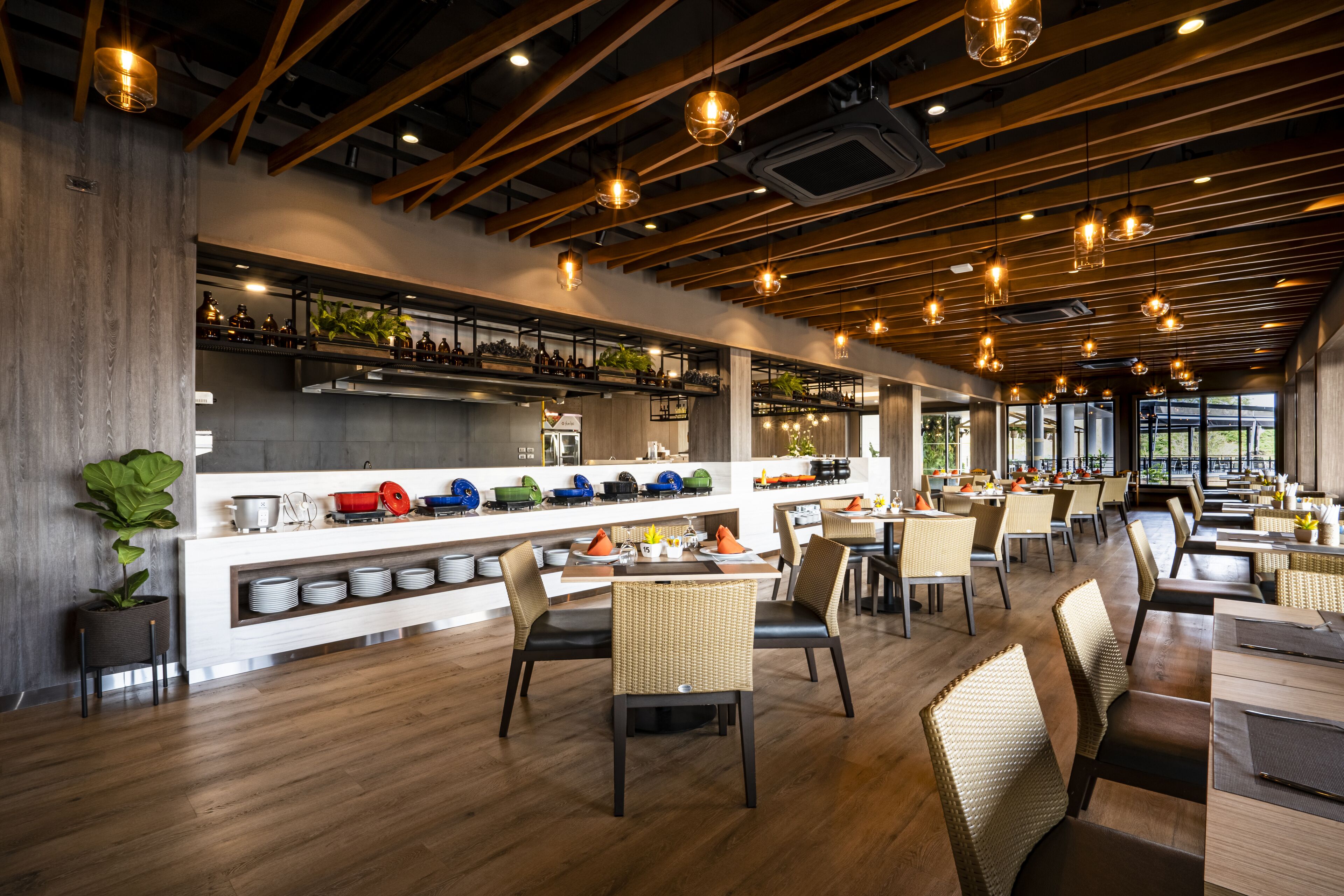 Een modern restaurant met een lange balie, meerdere zithoeken en een hoge plafond met zichtbare balken en hanglampen.