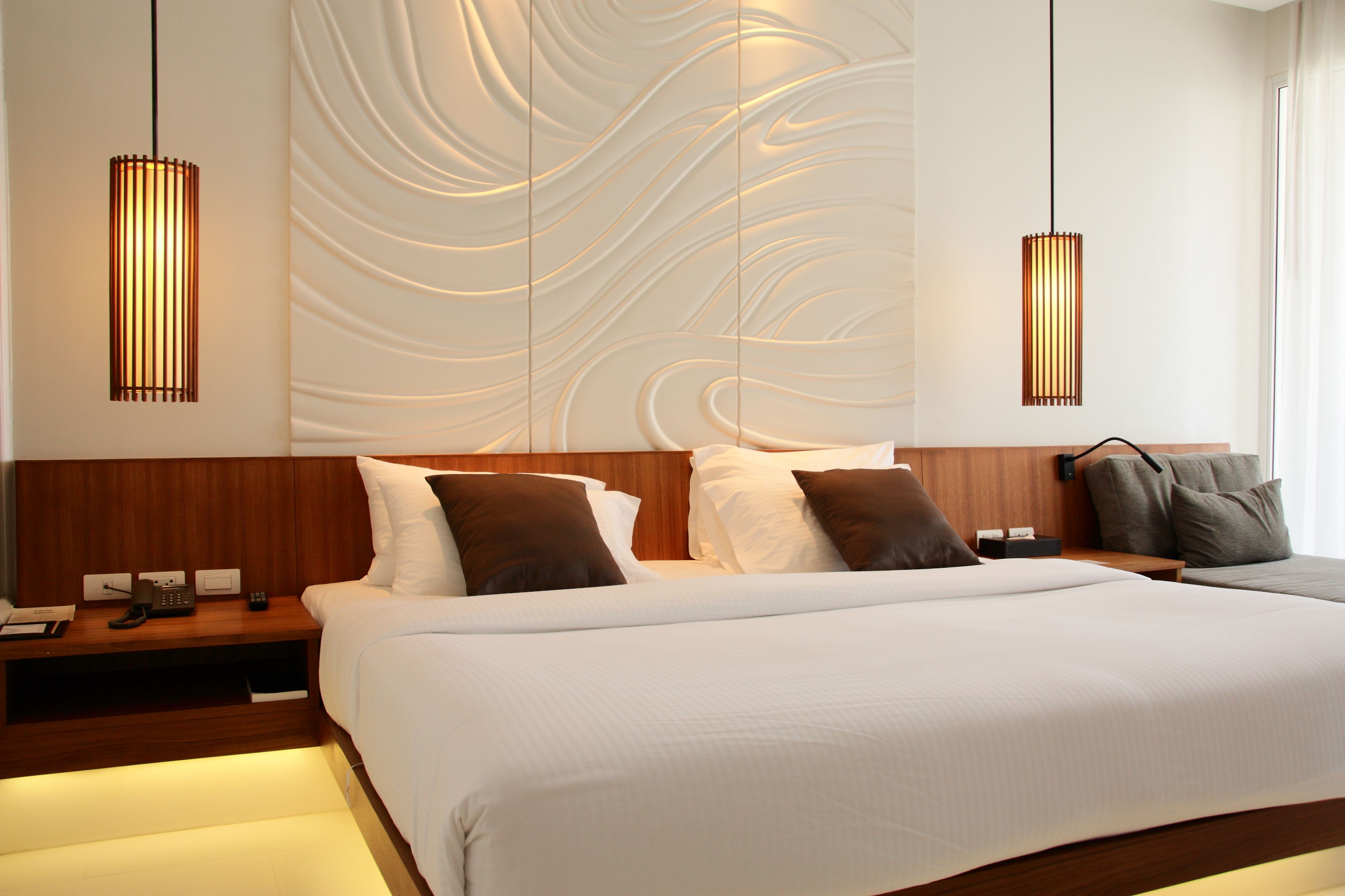 A modern hotel room with a large bed, wooden headboard, and two pendant lights.