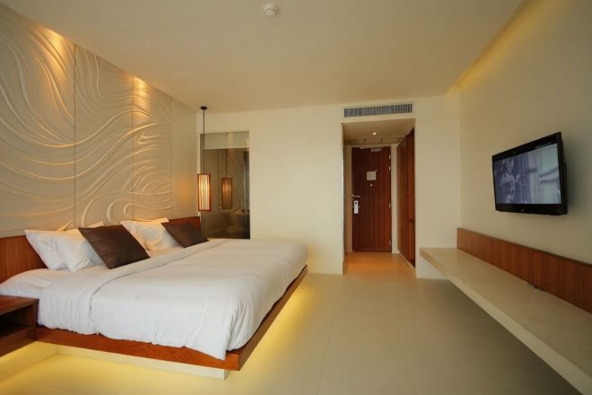 Una habitación de hotel moderna con una cama grande, un televisor de pantalla plana y un aplique de pared.