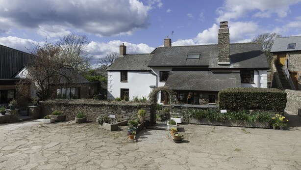 A traditional stone building with a white facade, a stone wall, and a paved courtyard with potted plants. - Burton Farmhouse (Kingsbridge)