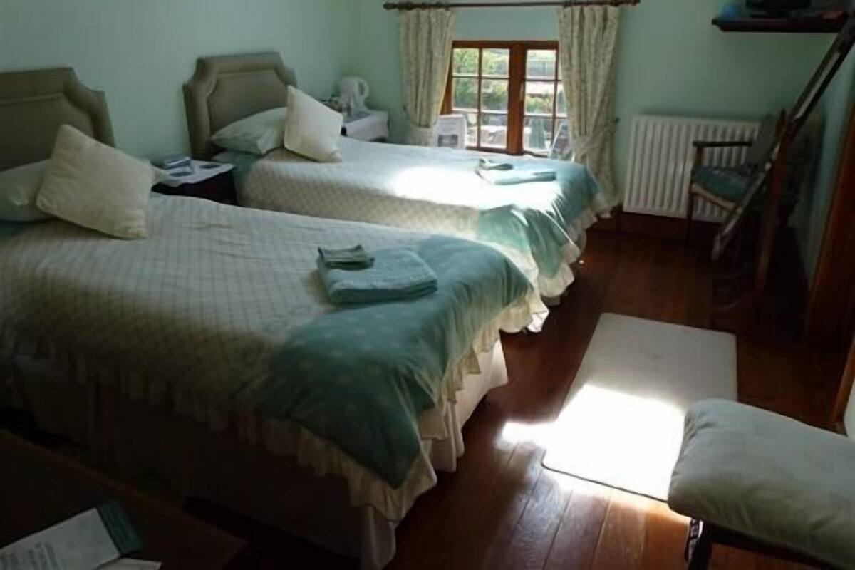 Una habitación con dos camas, una silla, un radiador y una ventana con cortinas.