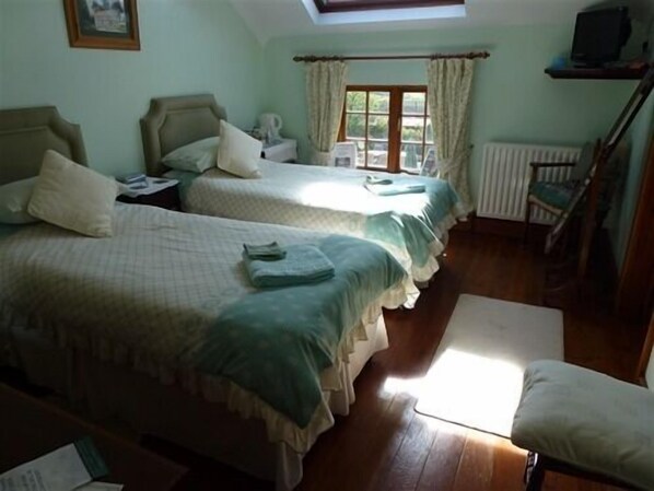 A room with two beds, a chair, a radiator, and a window with curtains. - Burton Farmhouse (Kingsbridge)