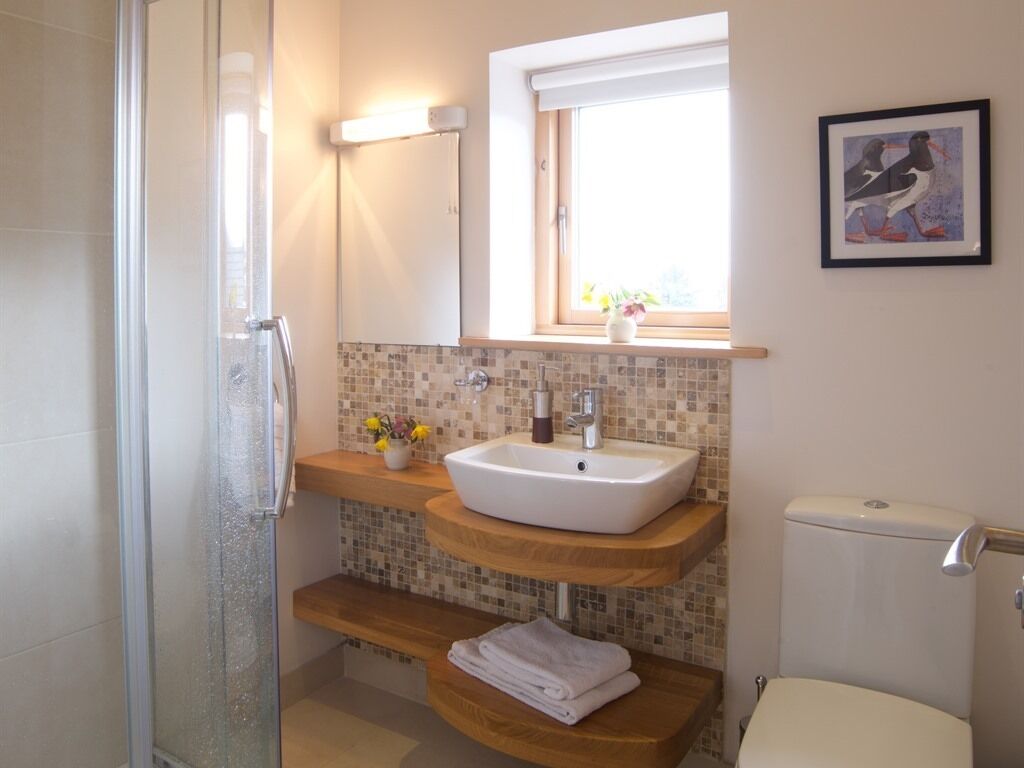 A bathroom with a glass shower enclosure, a white sink with a mosaic backsplash, and a toilet.