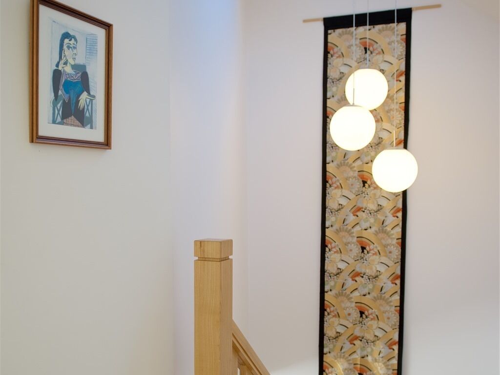 Un escalier avec une rampe en bois, une œuvre d’art encadrée au mur et un luminaire vertical doté de trois ampoules.