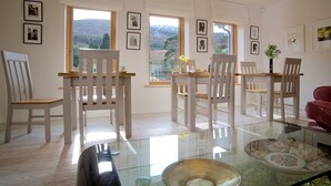 A spacious dining area with white chairs and a glass table, large windows offering a view of the outdoors, and framed pictures on the walls. - Cherryhill Lodge (Newcastle)