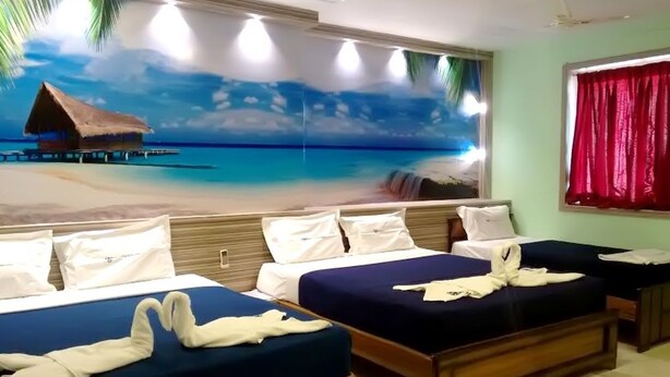Hotelkamer met een strandthema muurschildering, twee bedden, een houten hoofdbord en een raam met rode gordijnen.