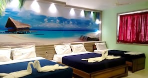 Une chambre d’hôtel décorée d’une fresque murale sur le thème de la plage, avec deux lits, une tête de lit en bois et une fenêtre ornée de rideaux rouges.