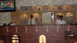 Een bar met een stenen muur, planken met flessen en een televisiescherm.