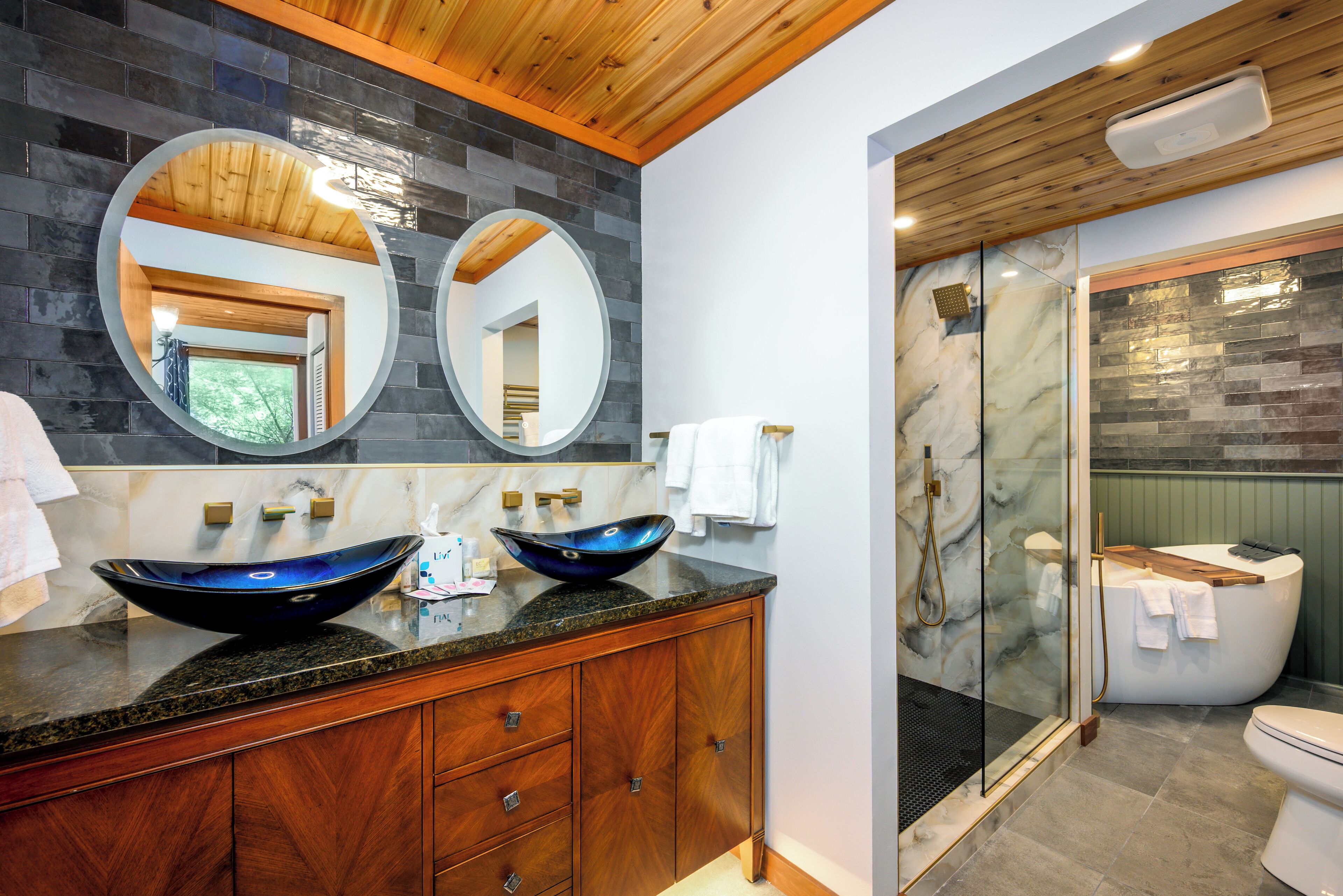 Une salle de bain moderne avec deux vasques sur pied, des meubles en bois et une douche séparée par une paroi de verre.