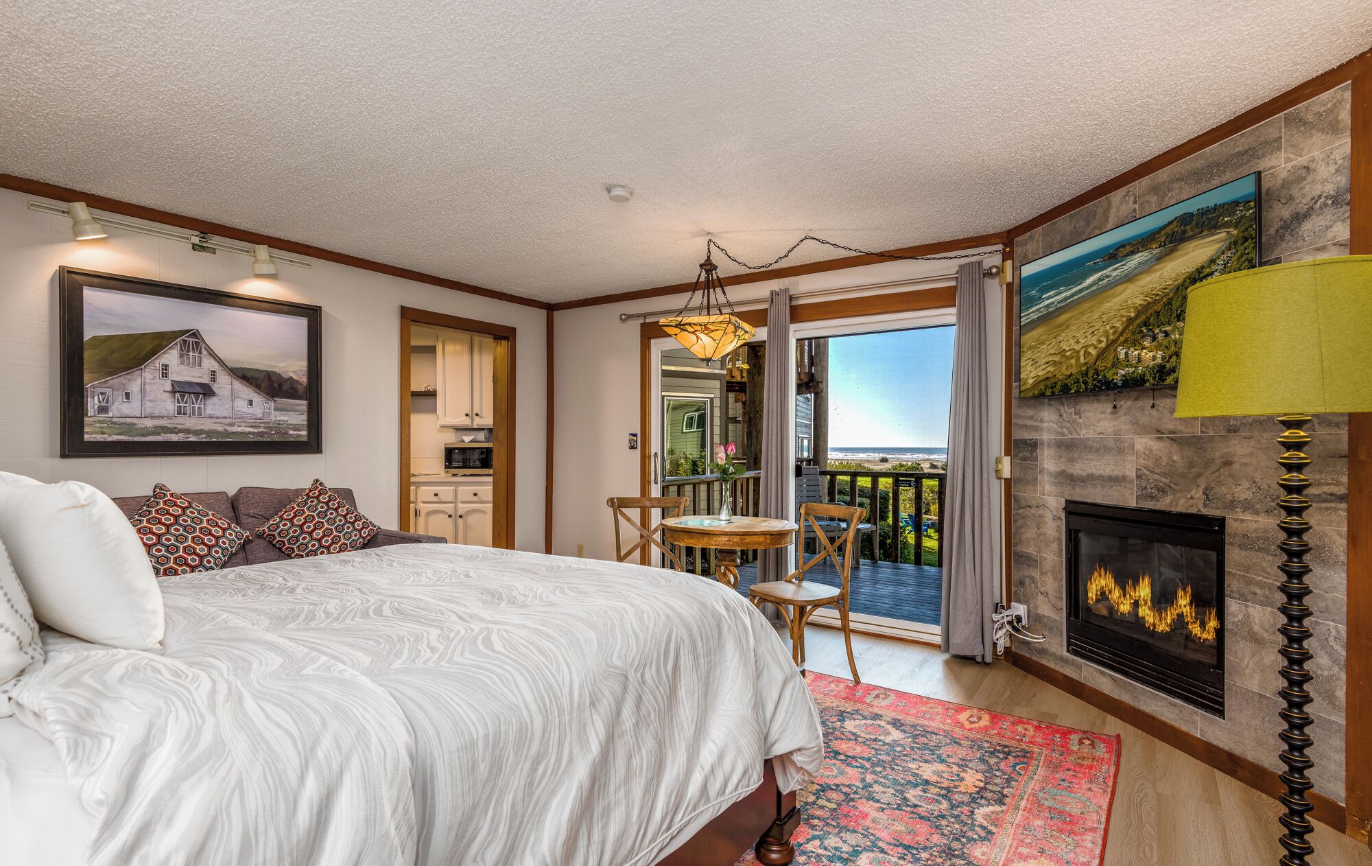 A bedroom with a bed, a fireplace, a dining area, and a view of the ocean.