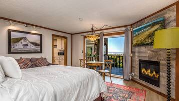 A bedroom with a bed, a fireplace, a dining area, and a view of the ocean.