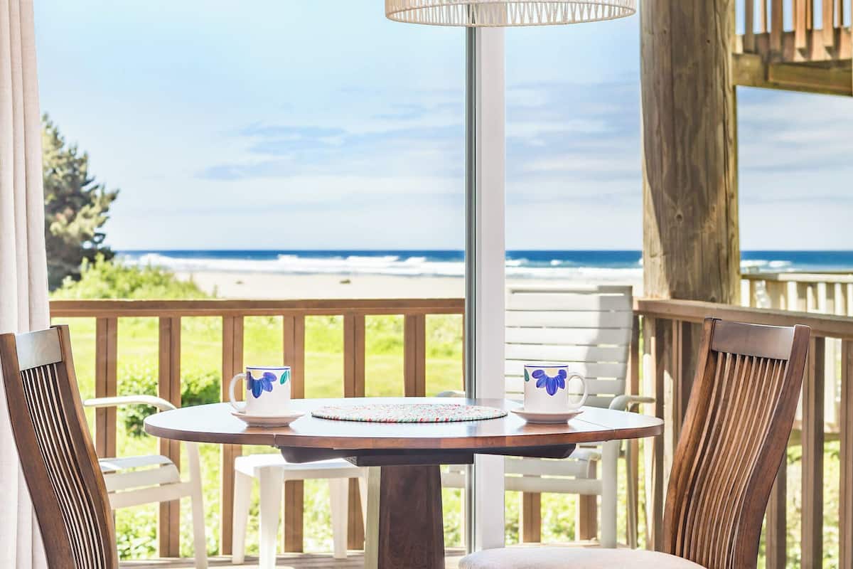 Una mesa redonda con dos tazas y platillos blancos, un posavasos tejido y vistas al océano.
