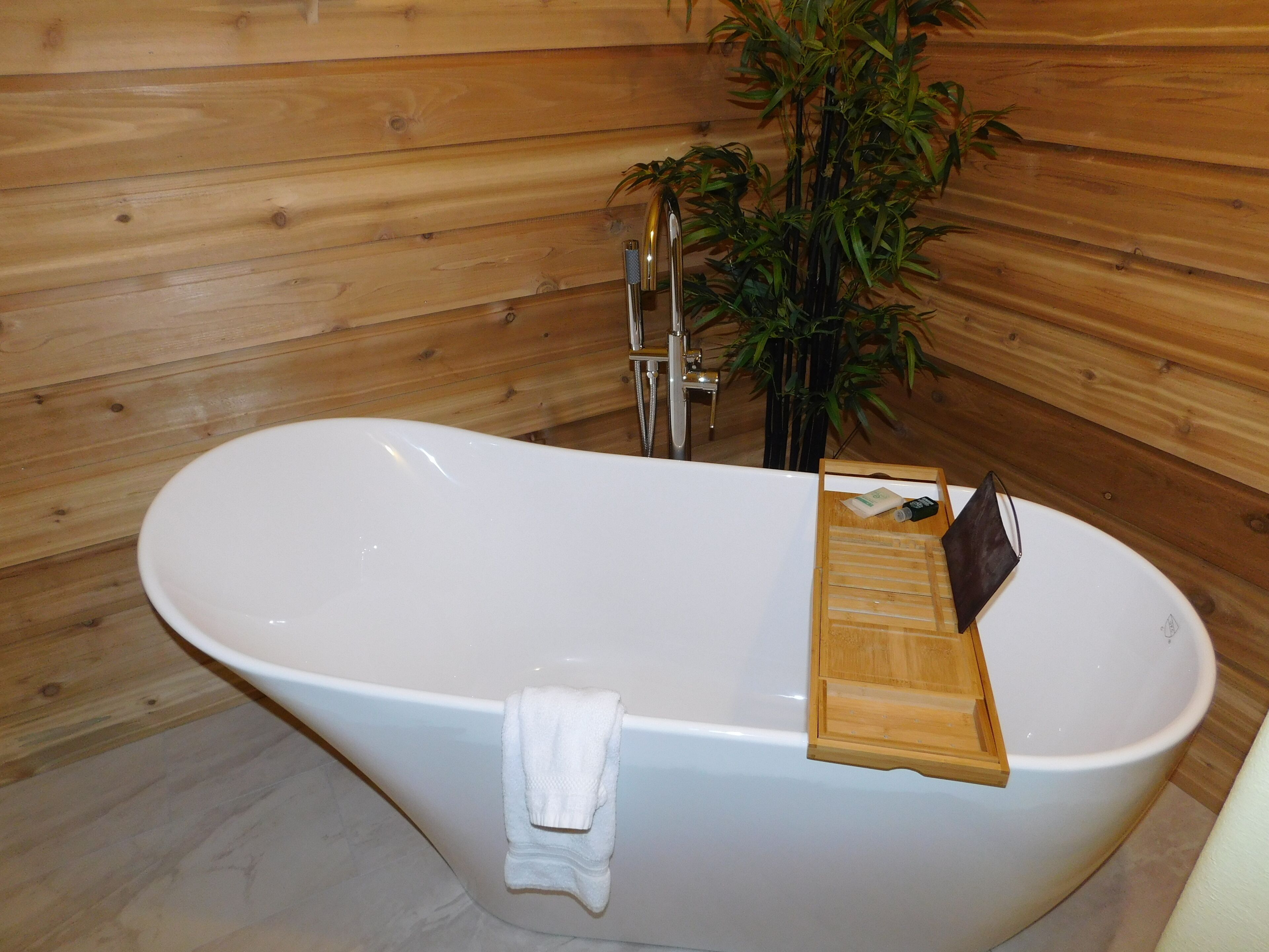 A wooden-paneled bathroom with a freestanding bathtub, a wooden tray, and a potted plant.