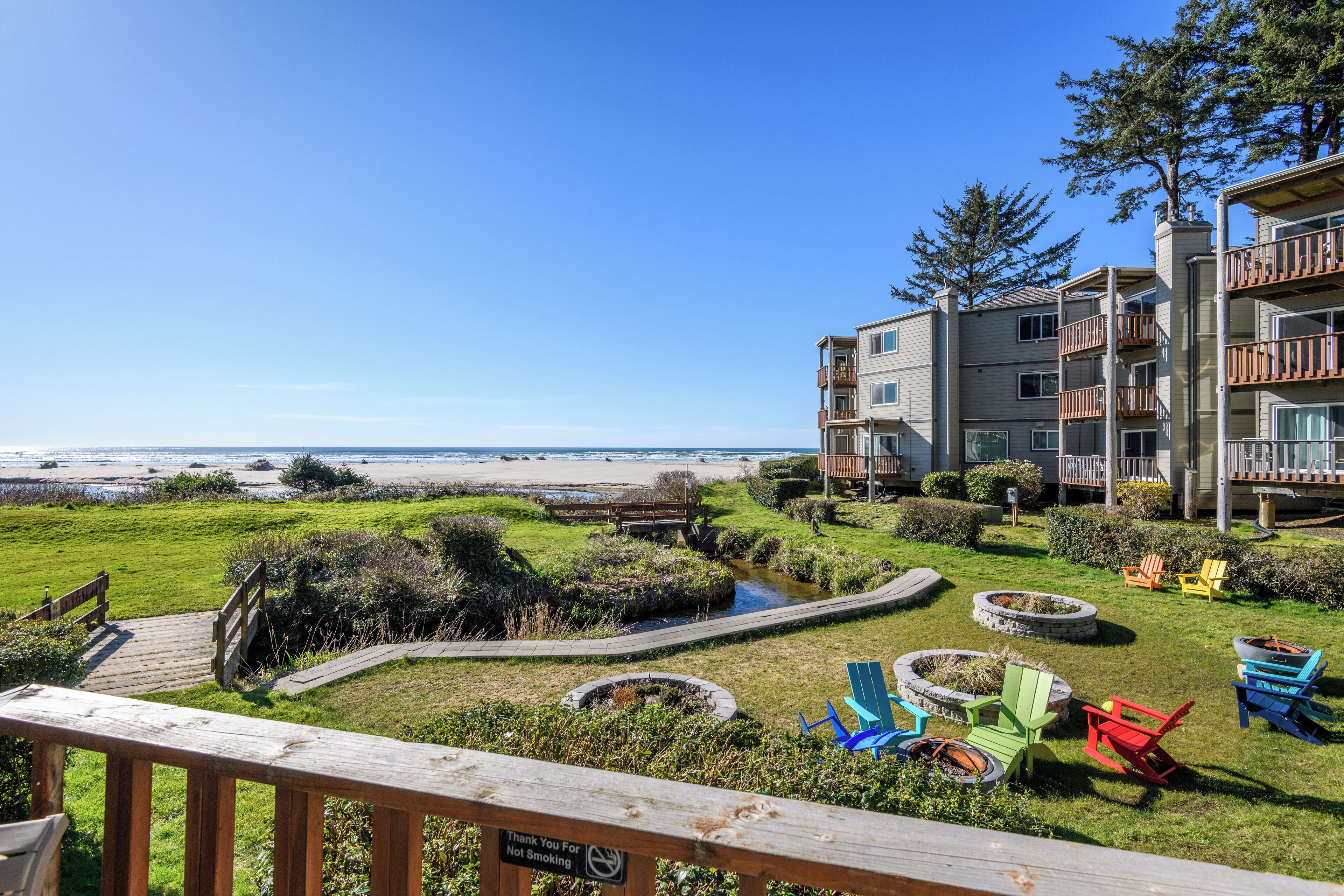 A view of a beachside property with a wooden deck, outdoor seating, and a clear view of the ocean.