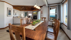 A dining area with a long wooden table, chairs, a decorative centerpiece, and a view of the ocean through large windows.