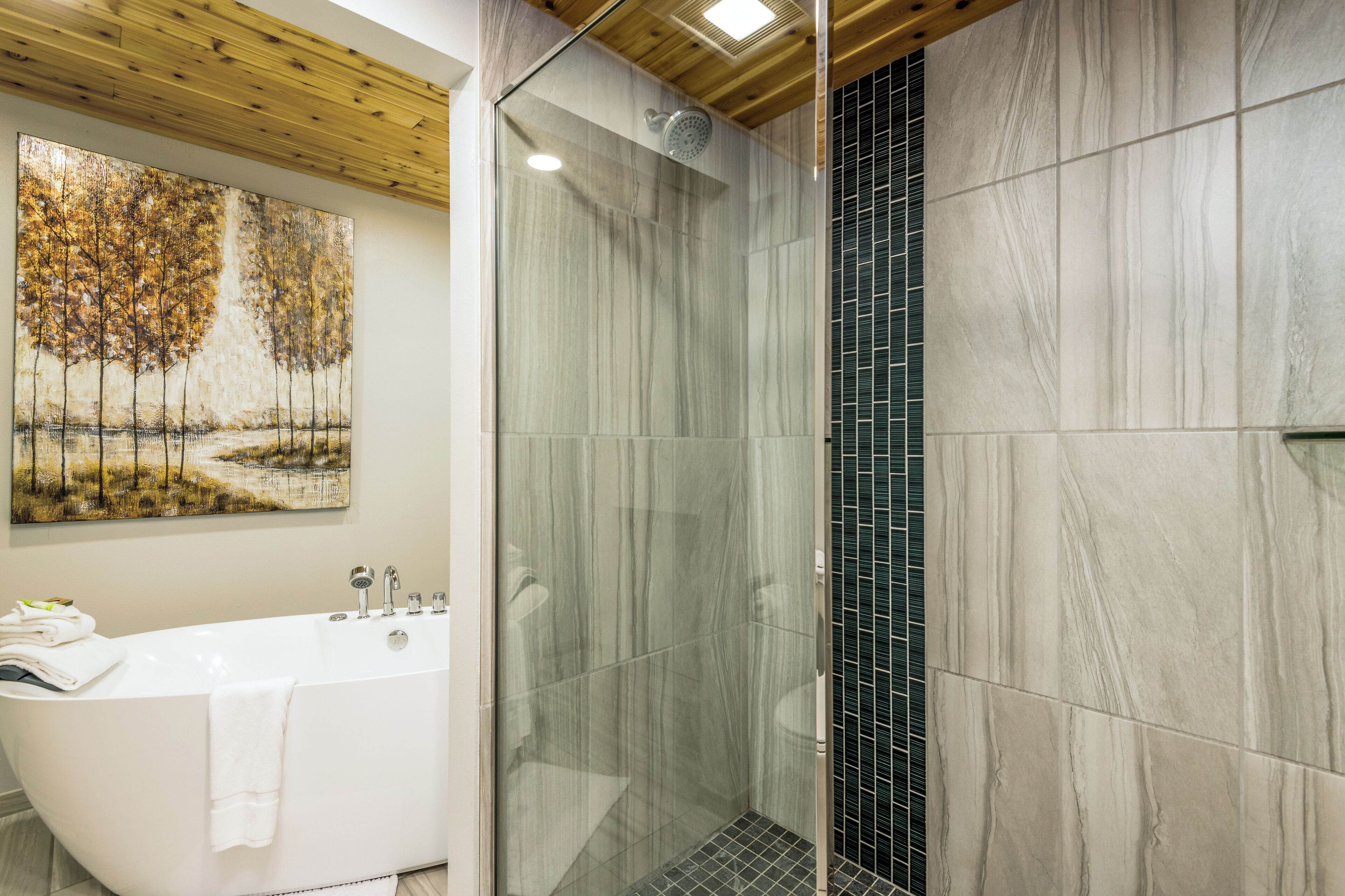 Un baño moderno con una bañera independiente, ducha con mampara de vidrio y un cuadro abstracto grande en la pared.