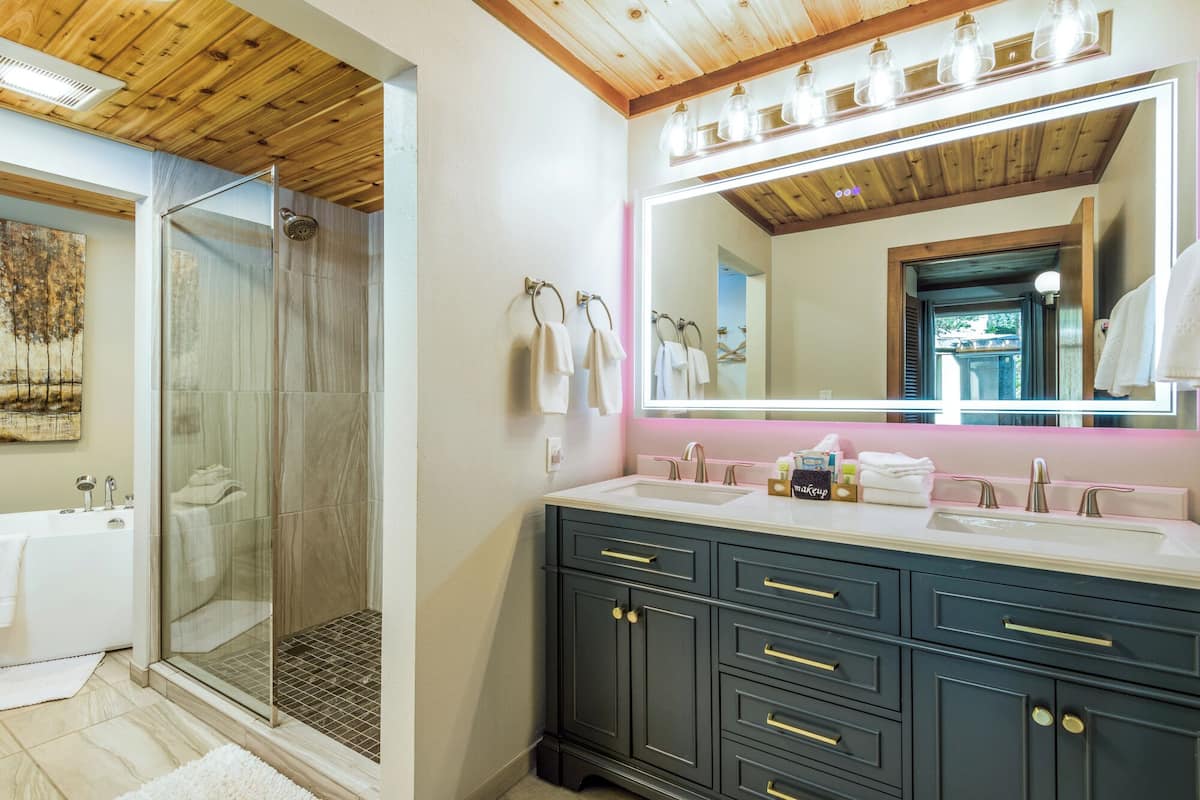 Un baño con cabina de ducha de vidrio, un espejo grande y muebles de color oscuro con tiradores dorados.