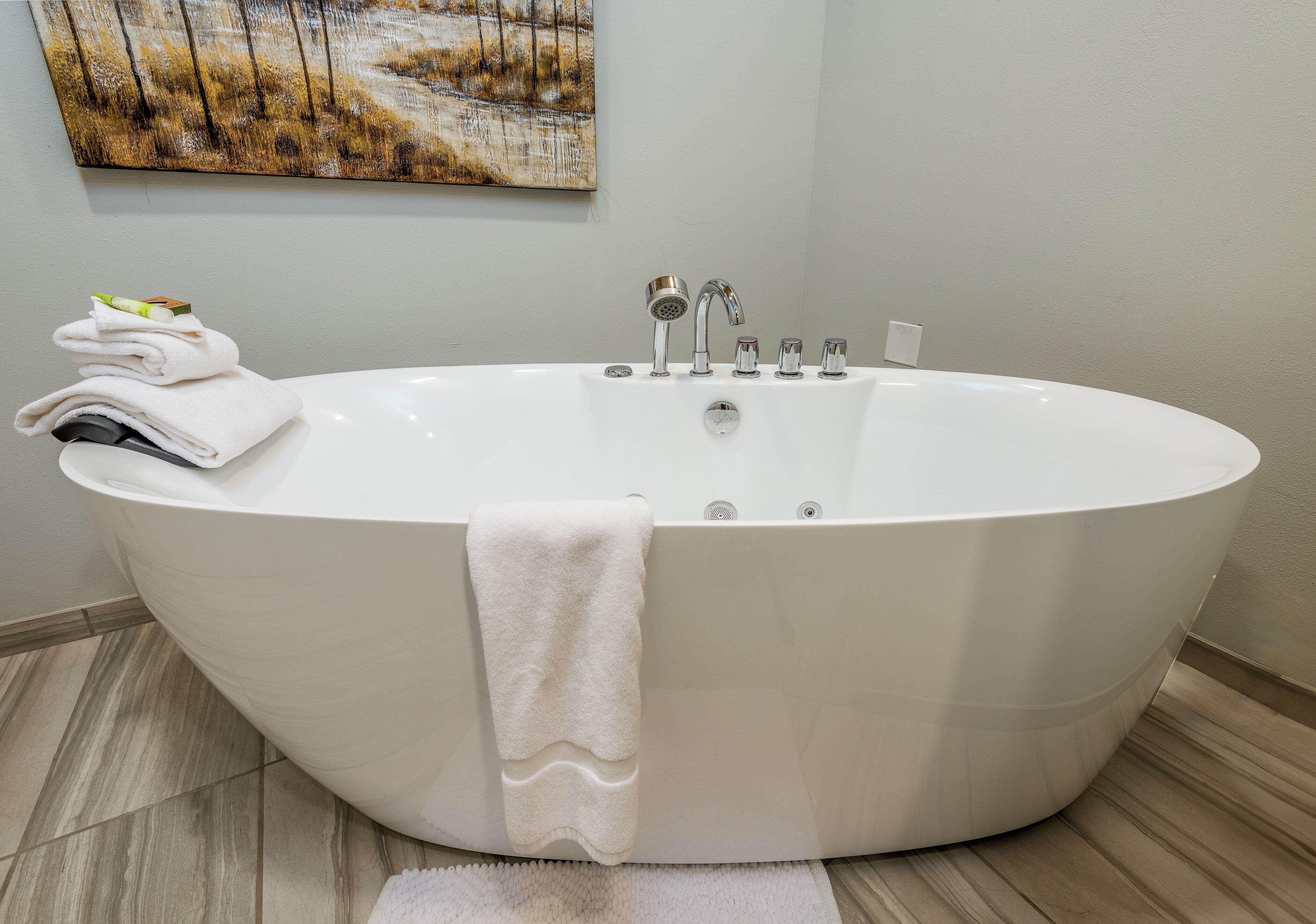 Een moderne badkamer met een vrijstaand bad, een stapel handdoeken en een schilderij aan de muur.