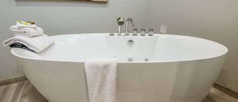Een moderne badkamer met een vrijstaand bad, een stapel handdoeken en een schilderij aan de muur.