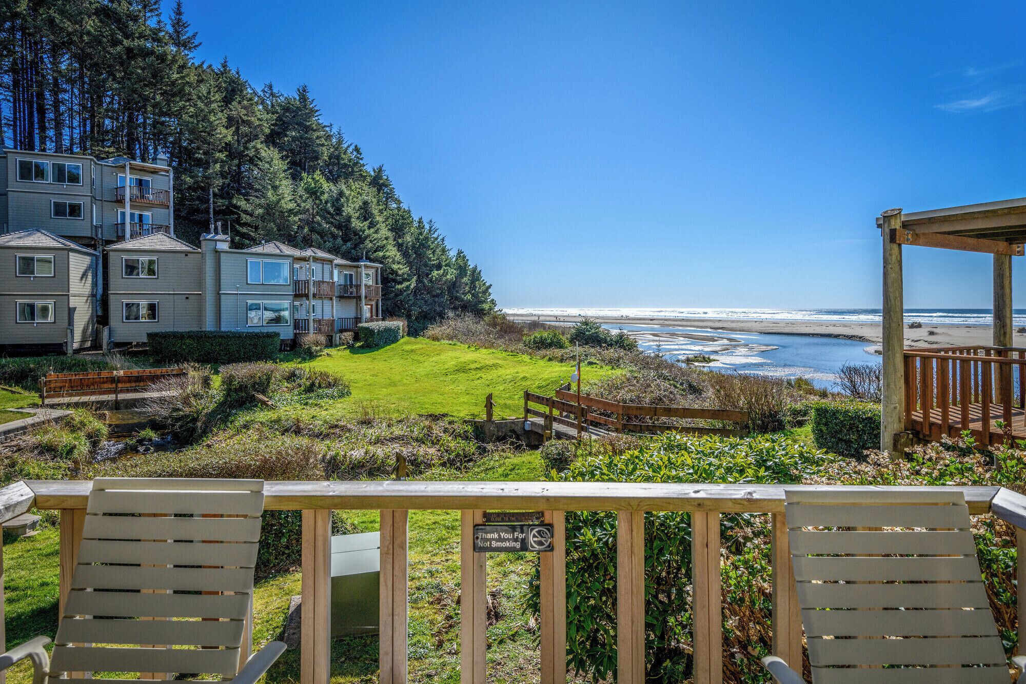 A coastal property with a view of the ocean, a grassy area, and wooden deck chairs.