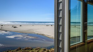 A beach view from a window, including the ocean, sandy beach, and some vegetation.