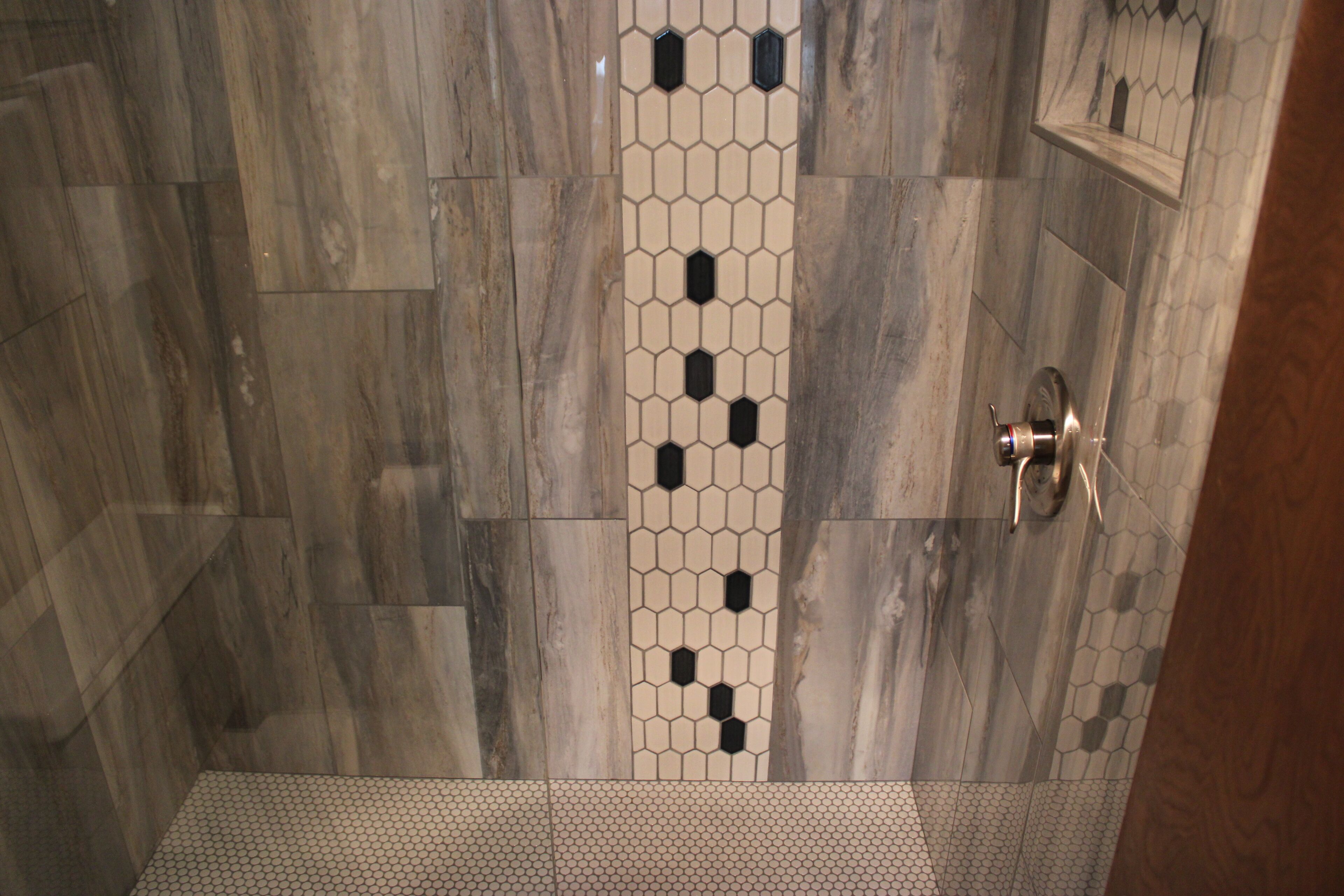 A shower area with a patterned tile design and a metallic door handle.