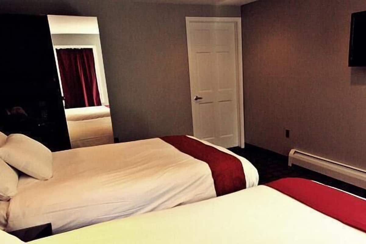 A hotel room with two beds, a door, a flat-screen TV, and a red curtain.