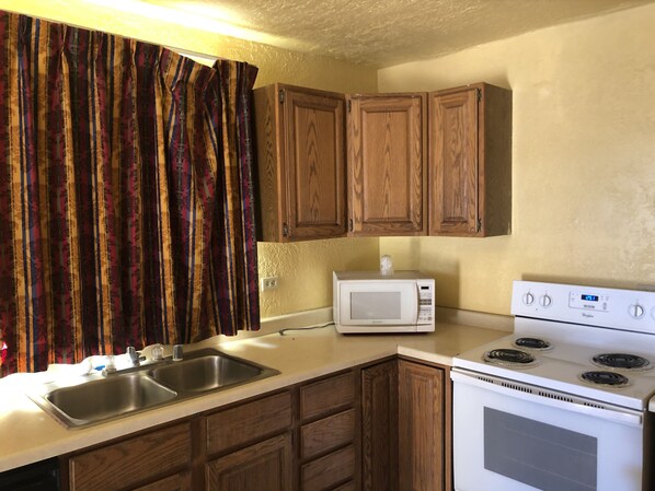 A kitchen with wooden cabinets, a white microwave, a stainless steel sink, and a white stove.