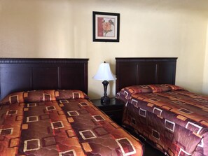 A hotel room with two beds, a nightstand with a lamp, and a framed picture on the wall.