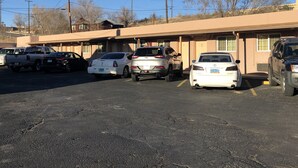 Un parking avec plusieurs voitures, un bâtiment dont les portes sont numérotées et un ciel dégagé.