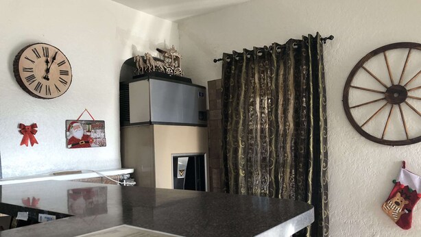 Une cuisine avec un plan de travail en granit, une horloge, un élément décoratif mural et un rideau.