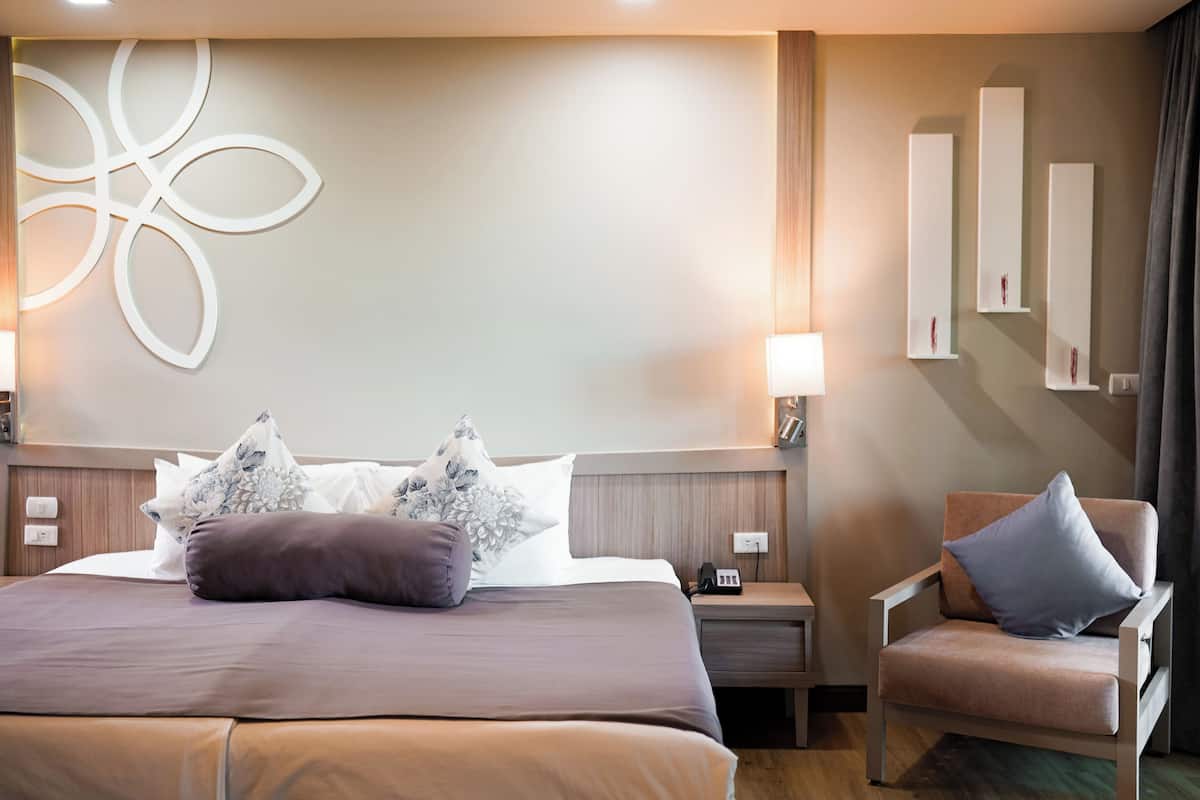 Ein Hotelzimmer mit einem großen Bett, einem Sessel, einem Nachttisch und Wandregalen.