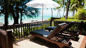 A sun lounger with a white umbrella, a wooden deck, and a view of the beach and ocean.