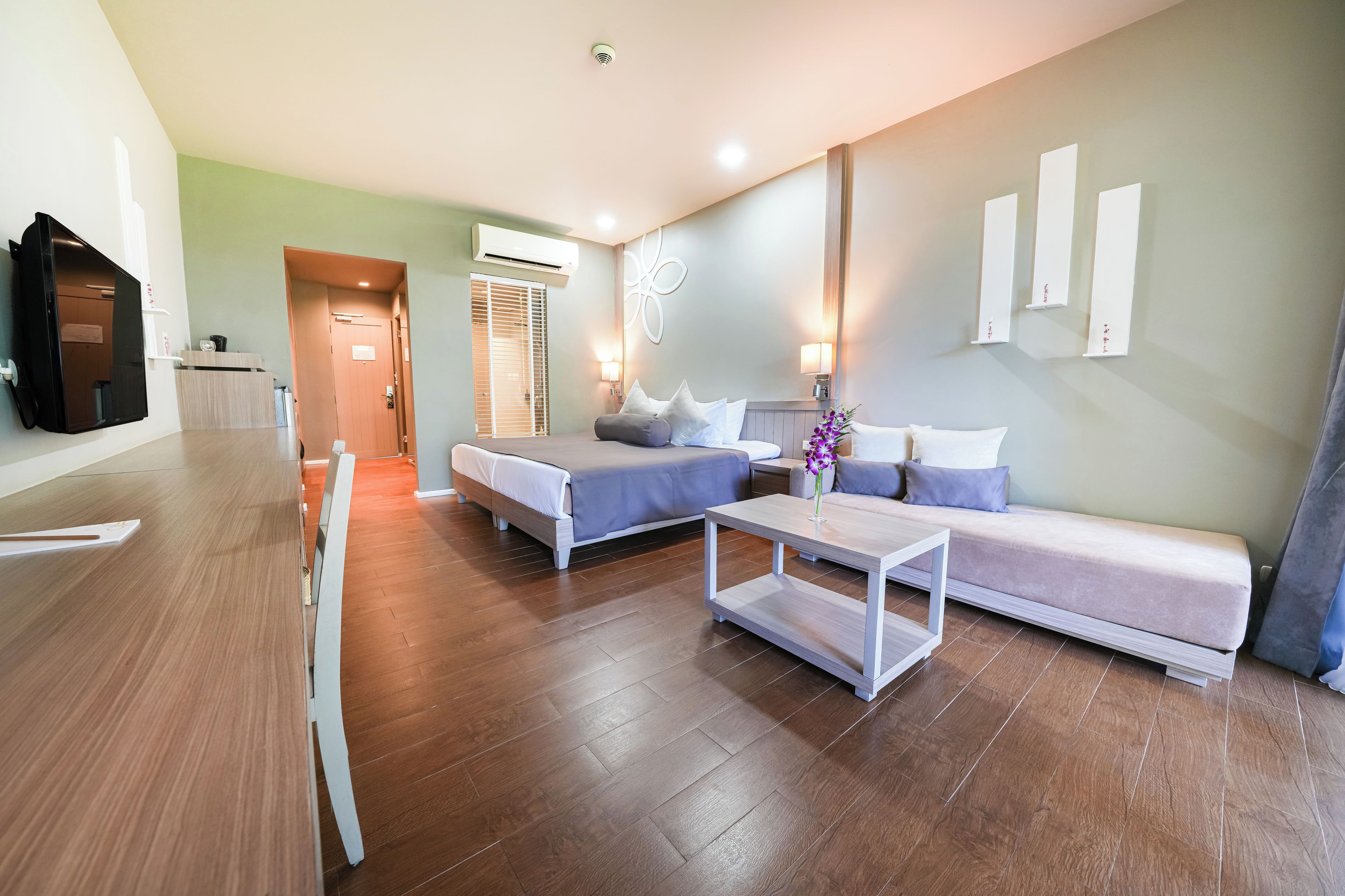 A modern hotel room with two beds, a sofa, a dining table, and a TV.