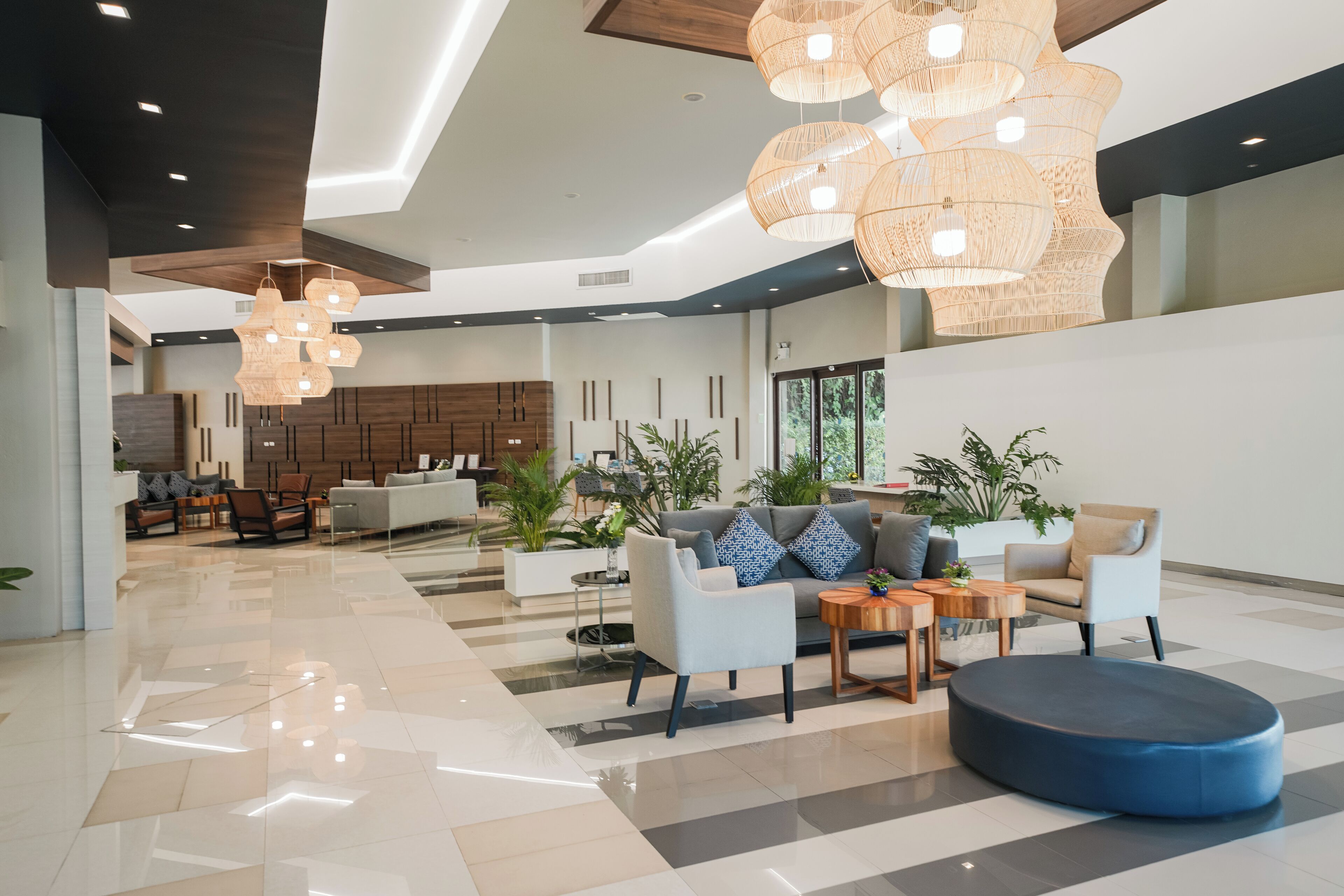 A spacious lobby with a modern design, featuring a reception desk, seating area with sofas and armchairs, and decorative lighting.