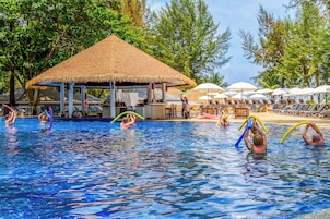 Zona de piscina con sillones de baño y sombrillas, rodeada de árboles.