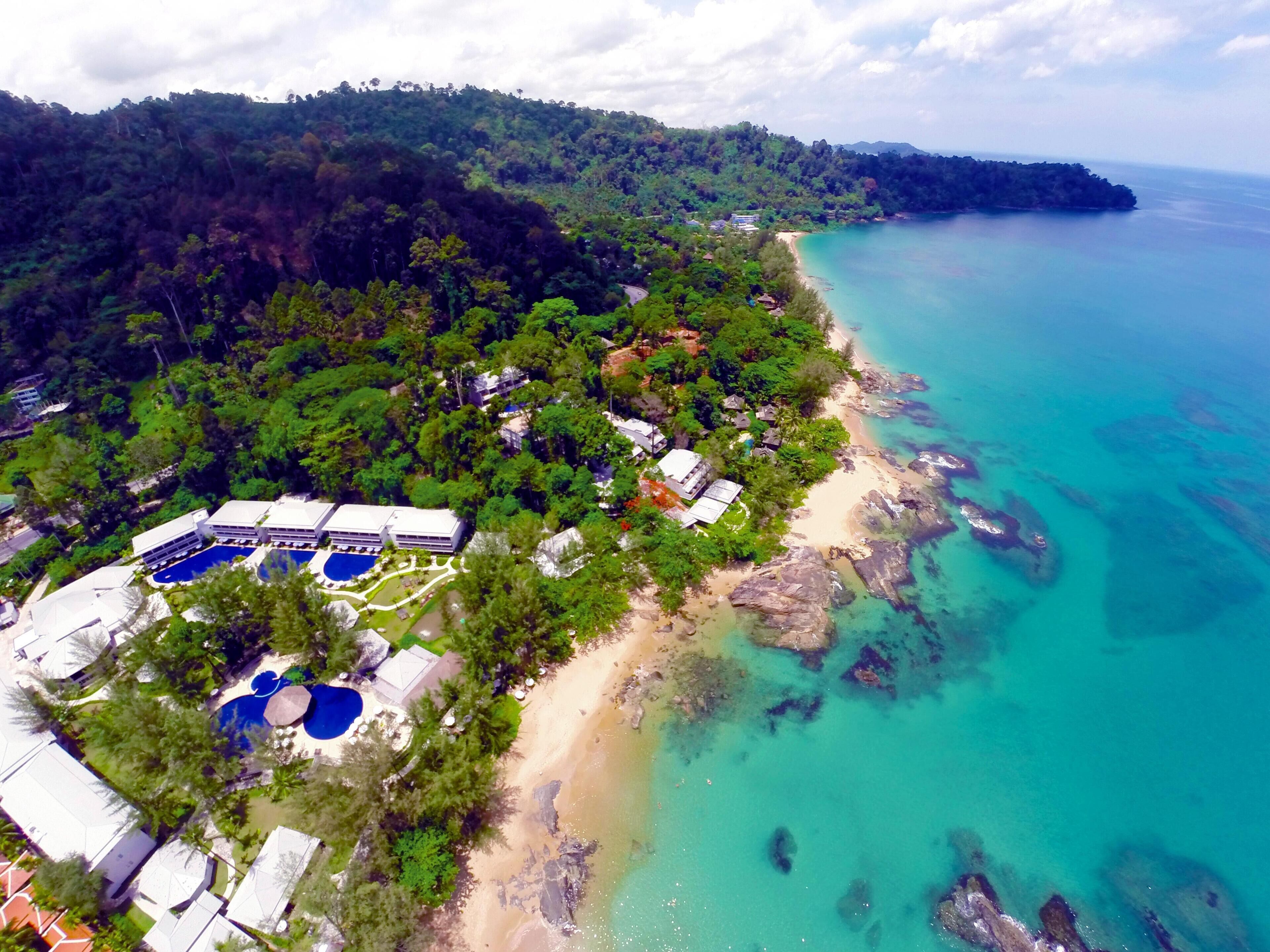 An aerial view of a resort with multiple buildings, a swimming pool area, and a beach adjacent to turquoise waters.