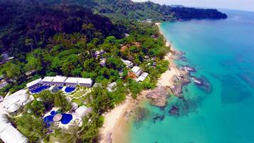 An aerial view of a resort with multiple buildings, a swimming pool area, and a beach adjacent to turquoise waters.