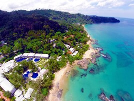 An aerial view of a resort with multiple buildings, a swimming pool area, and a beach adjacent to turquoise waters.