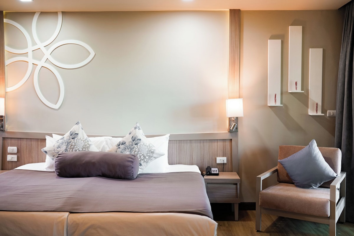 A hotel room with a large bed, a chair, a nightstand, and wall-mounted shelves.