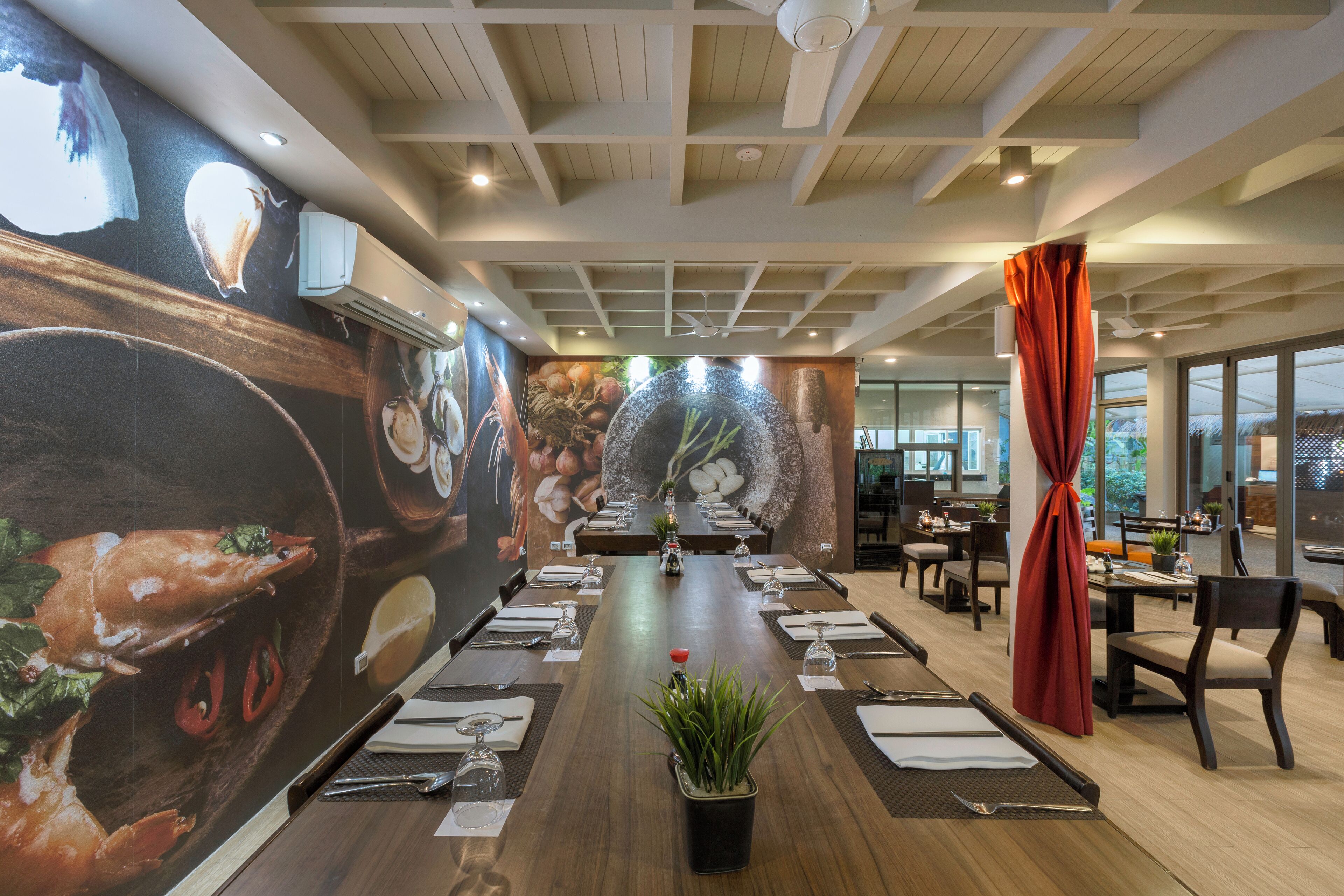 A conference room with a long table set for a meeting, surrounded by chairs, and a large mural depicting seafood on the walls.