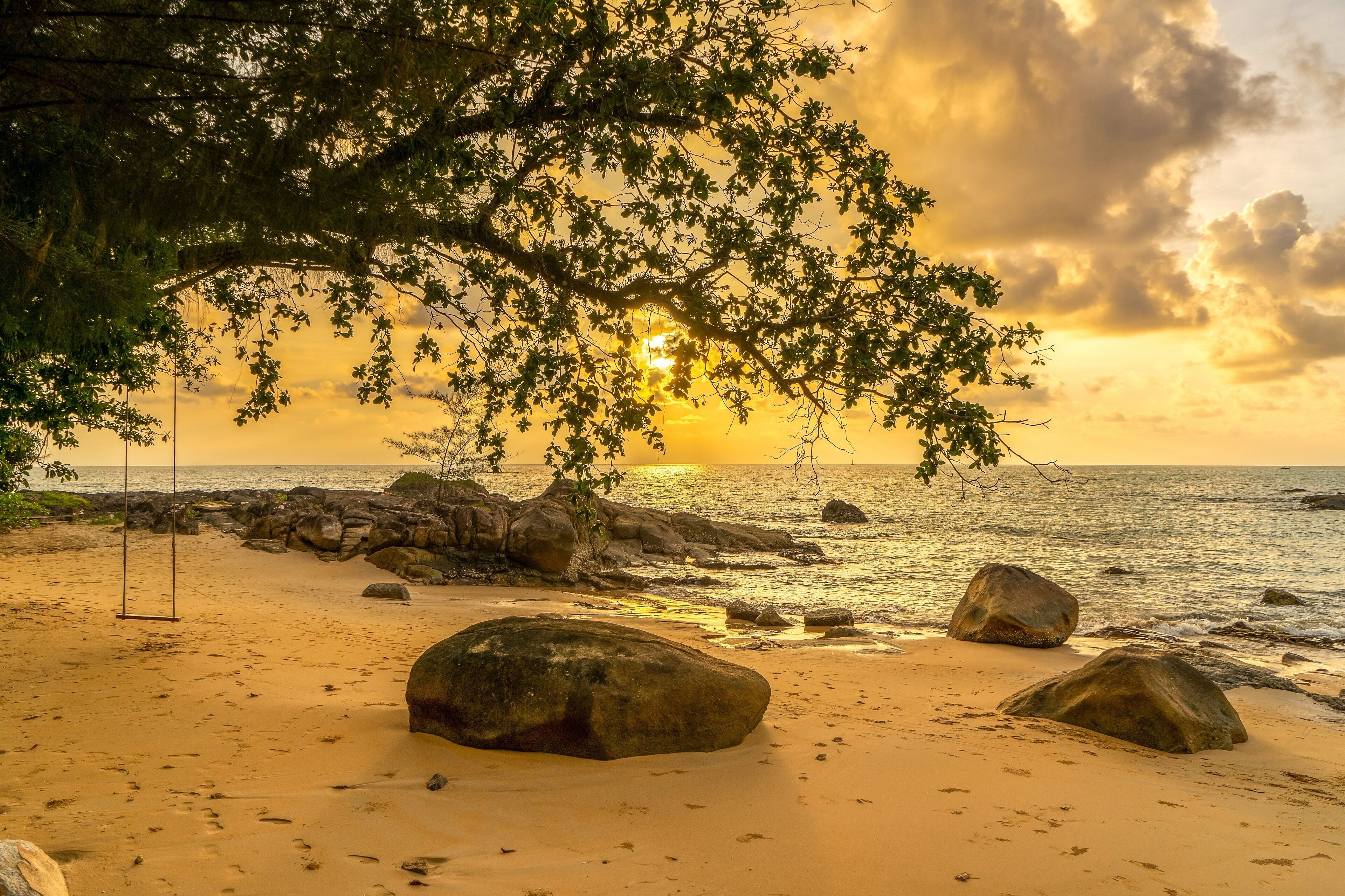A beach with large rocks, a swing, and a sunset view.