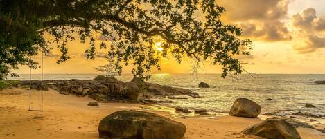 A beach with large rocks, a swing, and a sunset view.